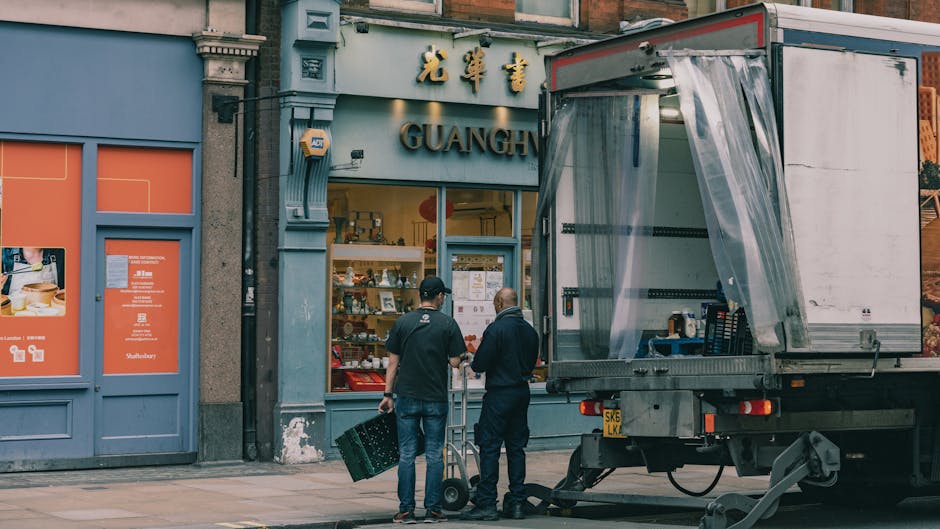 A busy street scene in Hale during daylight hours showing pedestrians walking along the pavement outside a row of retail shops including a hair salon named 'BARRY PALALA' with a black facade and large