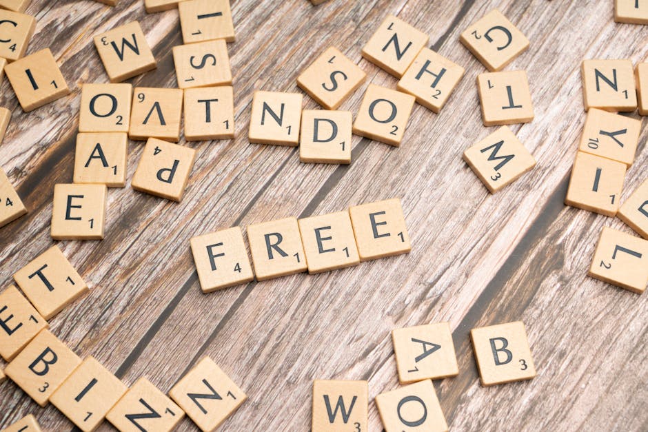 A collection of wooden Scrabble tiles arranged on a rustic wooden surface, spelling out the word 'FREE' in the center. Surrounding tiles include letters like E, T, A, B, W, and others, some scattered and some aligned in curved formations. The background showcases a natural, textured wood grain with visible splits and knots. This setup reflects themes of packing, sorting, and free offers related to house removals and moving services, which are part of the services provided by Man with Van The Hale. The scene captures the process of organizing or packing items for a home relocation, emphasizing careful handling and preparation in furniture transport and moving logistics.